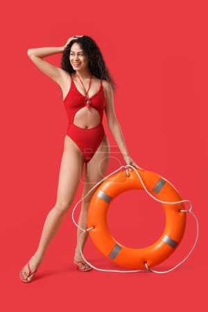 Photo for Beautiful young happy African-American female lifeguard with ring buoy on red background - Royalty Free Image