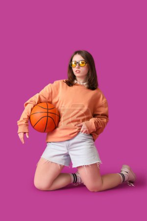 Mujer hermosa joven en ropa elegante con baloncesto sobre fondo púrpura