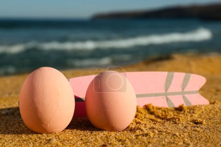 Painter Easter eggs and surfboard on sea beach