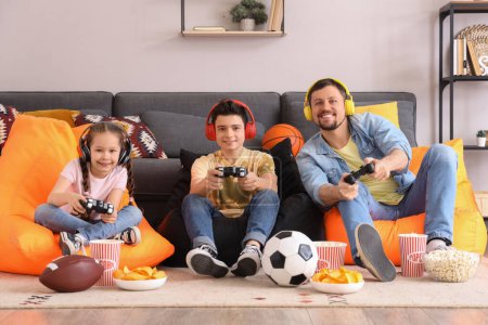 Père heureux avec ses petits enfants dans des écouteurs jouer à un jeu vidéo sur des sacs de haricots à la maison