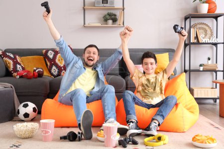 Joyeux petit garçon avec son père jouant à un jeu vidéo sur des sacs de fèves à la maison