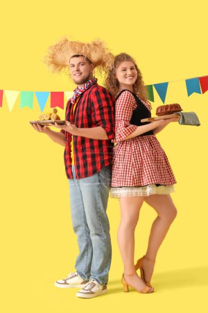 Glückliches junges Paar mit Fahnen, Mais und Kuchen auf gelbem Hintergrund. Festa Junina