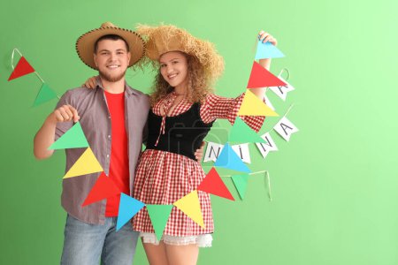 Glückliches junges Paar mit bunten Fahnen auf grünem Hintergrund. Festa Junina