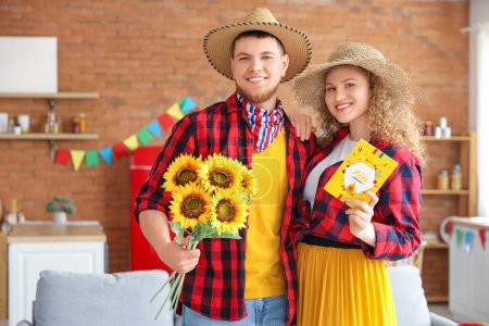 Glückliches junges Paar mit Sonnenblumen und Grußkarte zu Hause. Festa Junina