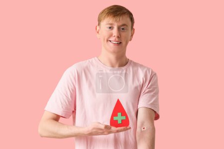 Donante de sangre masculino con parche aplicado y gota de papel sobre fondo rosa