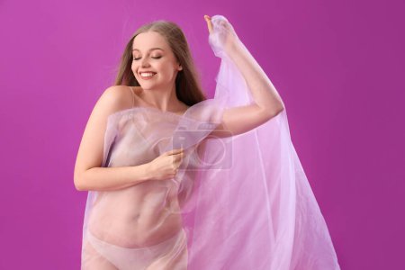 Beautiful young woman in underwear with fabric on purple background