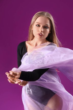 Beautiful young woman in bodysuit with fabric on purple background
