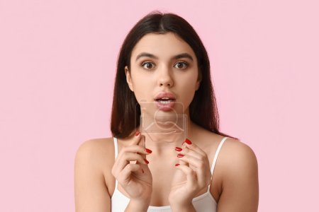Surprised young woman with lip mask on pink background
