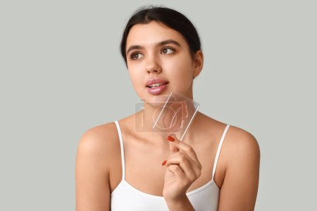 Beautiful young woman with lip mask on grey background