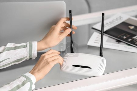 Woman with modern wi-fi router on table at home, closeup