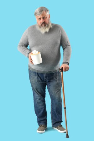 Photo for Portrait of sad senior man with tissues and walking stick on blue background - Royalty Free Image