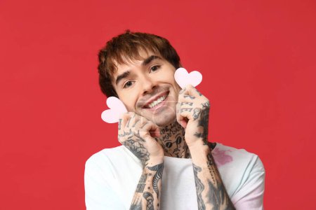 Handsome young man with paper hearts on red background