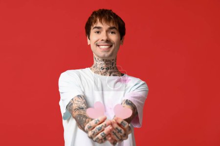 Handsome young man with paper hearts on red background