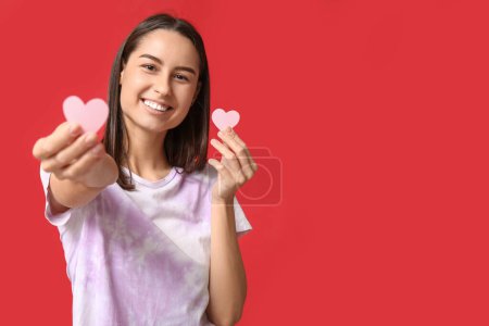 Beautiful young woman with paper hearts on red background