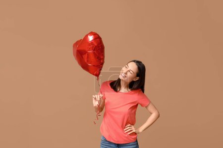 Hermosa mujer joven con globo de aire en forma de corazón sobre fondo beige