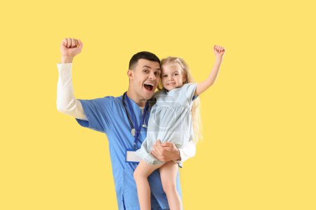 Cheerful male pediatrician with little girl on yellow background