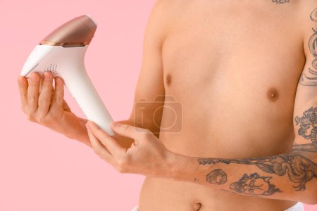 Young man with photoepilator on pink background, closeup
