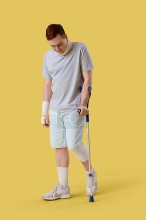 Verletzter junger Mann nach Unfall mit Krücke auf gelbem Grund