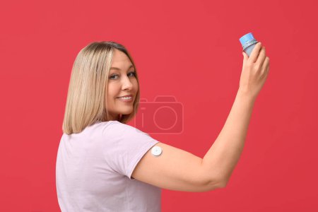 Femme avec capteur de glucose pour mesurer le taux de sucre dans le sang et applicateur sur fond rouge. Concept de diabète