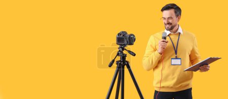 Male journalist with microphone and clipboard recording video on yellow background with space for text