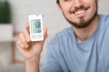 Diabetic young man using glucometer at home, closeup