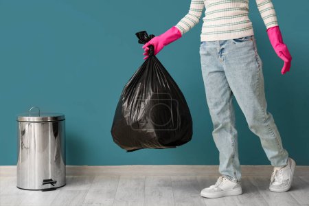 Woman with garbage bag and trash bin near blue wall