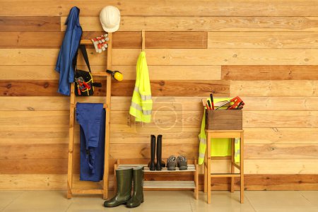 Téléchargez les photos : Gilets de sécurité, uniformes, outils et chaussures près du mur en bois - en image libre de droit