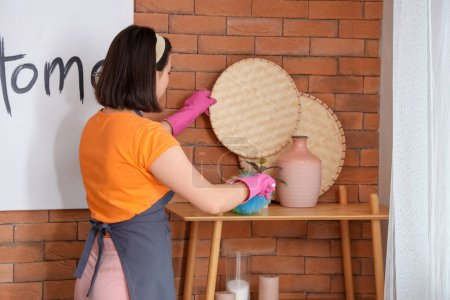 Young woman cleaning wooden rack with pp-duster at home