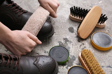 Hands cleaning shoes with cloth on grey grunge background