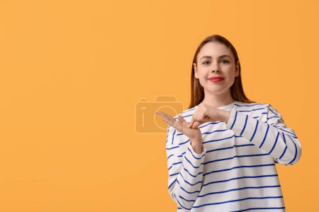 Young deaf mute woman using sign language on orange background
