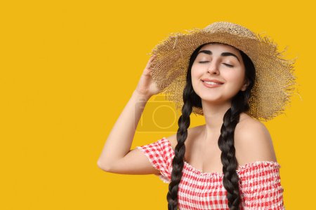 Schöne junge glückliche Frau mit Strohhut auf gelbem Hintergrund. Fest Junina (Juni-Fest)