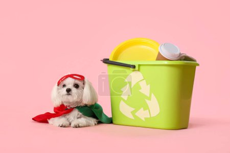 Niedlicher kleiner Hund im Öko-Superheldenkostüm mit Mülleimer und Müll auf rosa Hintergrund