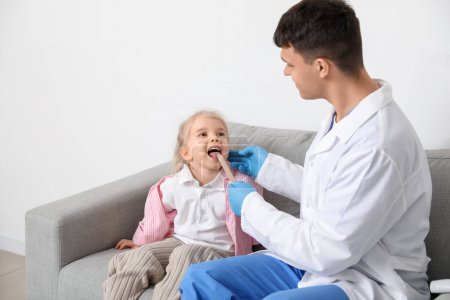 Male pediatrician examining little girl with tongue depressor in clinic