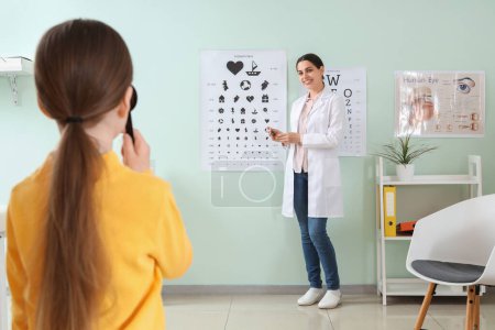 ophtalmologiste féminine vérifiant la vue de la petite fille près de la carte de test à la clinique