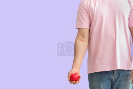 Blood donor with applied medical patch holding heart on lilac background