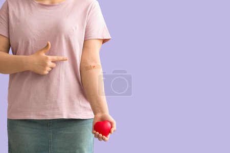 Blood donor with heart pointing at applied medical patch on lilac background