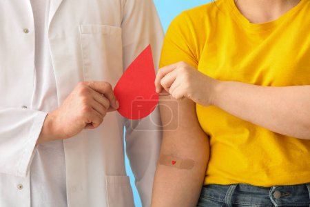 Doctor and donor with applied medical patch holding paper blood drop on blue background