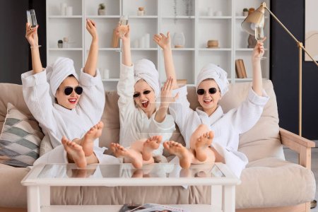 Happy young woman and her bridesmaids with champagne on sofa at Hen Party