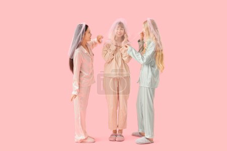 Young woman and her bridesmaids in pajamas on pink background. Hen Party