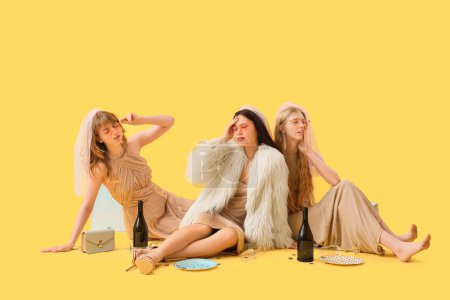 Young Asian woman and her bridesmaids with hungover on yellow background. Hen Party