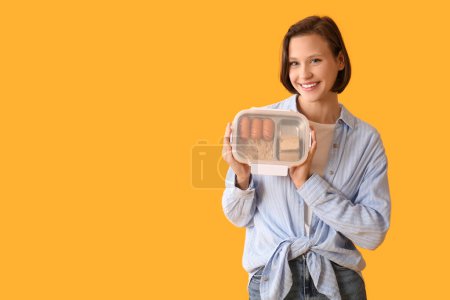 Beautiful young happy woman with lunchbox of tasty food on yellow background