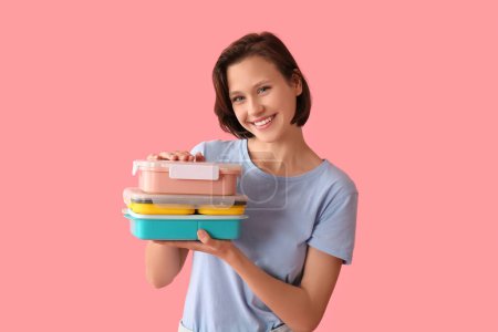 Beautiful young happy woman with lunchboxes of tasty food on pink background