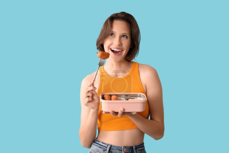 Beautiful young happy woman with lunchbox of tasty food on blue background