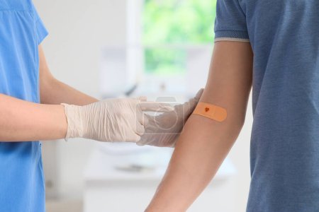 Nurse pointing at applied medical patch on blood donor's arm in clinic, closeup