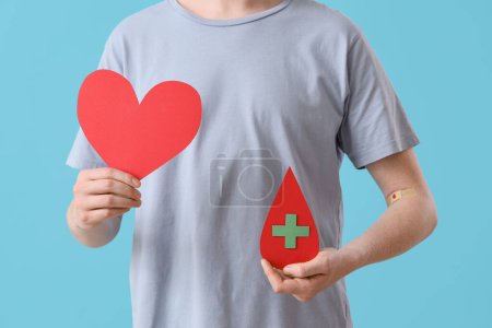 Male blood donor with paper heart and drop on blue background, closeup
