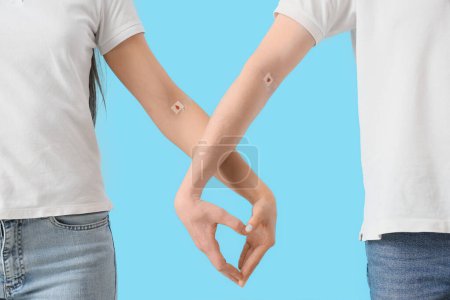 Blood donors with applied patches making heart gesture on blue background, closeup