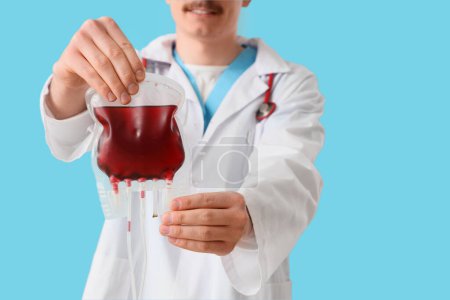 Male doctor with blood pack for transfusion on blue background, closeup