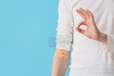 Male blood donor with applied patches showing OK on blue background, closeup
