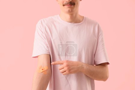 Male blood donor pointing at applied patches on pink background, closeup