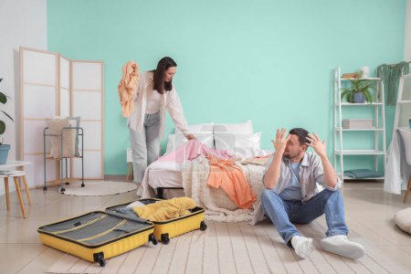 Téléchargez les photos : Upset young woman packing clothes and her husband in bedroom. Cheating concept - en image libre de droit